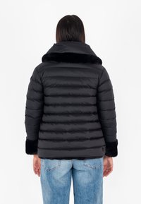 Giacca a vento nera con design a righe orizzontali, colletto e polsini in pelliccia sintetica e orlo elastico. Indossata sopra jeans blu chiaro.