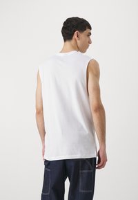 Hvid ærmeløs bomulds t-shirt med en afslappet pasform, rund halslinje og lige kant, båret med mørke denim cargo bukser.