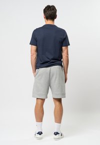 T-shirt en coton bleu marine associé à un short en jersey gris clair. Le modèle porte des chaussettes blanches et des baskets blanches avec des accents bleus. Design simple, coupe décontractée.