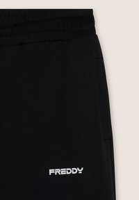 Pantalon de survêtement noir avec une taille élastique, arborant un logo "FREDDY" en blanc. Texture lisse avec des poches latérales pour plus de fonctionnalité.