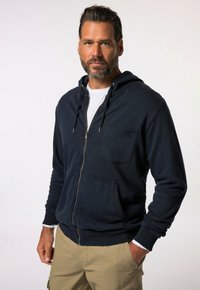 Navy blue zip-up hoodie, featuring a front pocket, drawstring hood, and ribbed cuffs and hem. Fabric appears textured and soft.