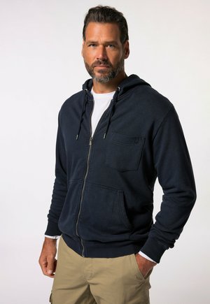 Marineblauwe zip-up hoodie, met een voorzak, trekkoorden in de capuchon en ribgebreide manchetten en onderrand. De stof lijkt textuur te hebben en is zacht.