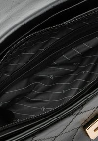 Interno di borsa a tracolla in ecopelle nera con compartimento con cerniera. Foderata in tessuto nero con motivo a strisce grigie e dettagli con logo.