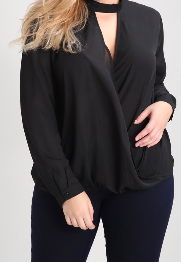 Femme portant un chemisier noir à manches longues avec un col en trou de serrure et un détail noué à l'avant, associé à un pantalon ajusté foncé.