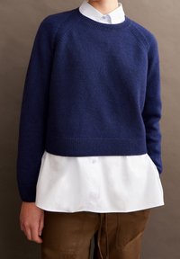 Marineblauwe wollen trui met een geribde ronde hals, cropped ontwerp, raglanmouwen, gedragen over een wit overhemd met kraag en een bruine broek.