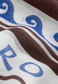 Gros plan sur un tissu à rayures brunes et motifs tourbillonnants bleus sur fond blanc, montrant la texture et les plis.