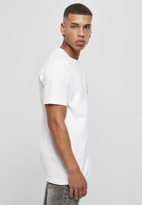 Hvid bomulds T-shirt med afslappet pasform, rund hals og korte ærmer, med et lille multfarvet grafisk motiv på brystet.