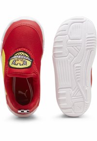 Piros slip-on cipők puha szövet felsőrésszel, sárga díszítéssel és fekete-sárga logópatch-csel. Fehér gumitalp, amely texturált tapadást biztosít.