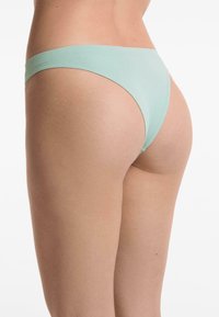 Dunne, mintgroene bikini slip met een laag uitgesneden tailleband en minimale achterkantbedekking. Zachte stoftextuur, eenvoudig ontwerp, geen zichtbare patronen.