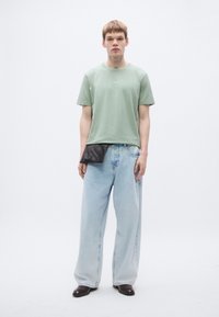 Light green cotton t-shirt with a crew neck and subtle logo, paired with loose blue denim jeans and black leather pouch detail.