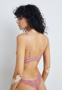 Lace lingerie set in soft pink, featuring thin satin straps, a hook-and-eye back closure, and scalloped edges on the bra and thong.