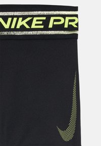 Shorts de sport noirs avec une large ceinture réfléchissante jaune néon portant le texte "NIKE PRO" et un accent logo à rayures diagonales.