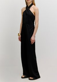 Schwarzer Halfter-Overall aus leichtem Material, mit einem taillierten Oberteil und lockeren, fließenden Beinen. Einfaches Design mit minimalen Details.