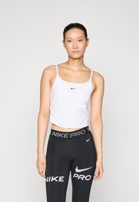 Valge lühike tank top, millel on õhukesed rihmad, esitleb väikest musta Nike logo. Kombineeritud mustade legginsitega, millel on vööl "NIKE PRO" bränding.