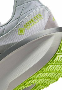 Sneaker grigio con il logo Gore-Tex in verde, suola arrotondata, tomaia testurizzata e suola di trazione verde brillante.