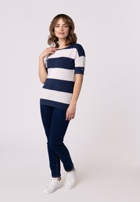 Haut rayé bleu marine et crème, manches courtes, col rond. Associé à un jean skinny bleu foncé et des baskets blanches. Design minimaliste.
