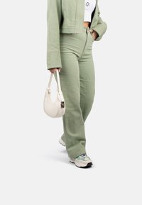 Veste verte courte avec des coutures contrastantes, pantalon large assorti et sac à main en cuir blanc. Baskets à design texturé.