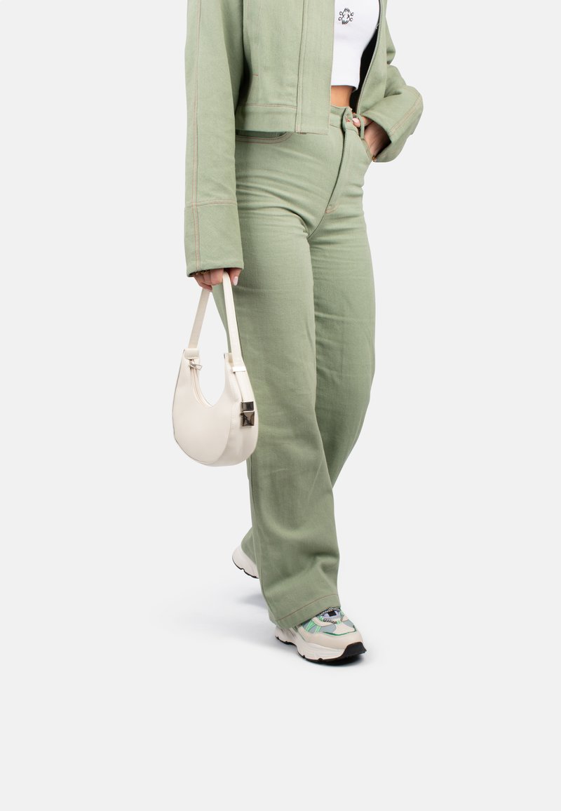 Veste verte courte avec des coutures contrastantes, pantalon large assorti et sac à main en cuir blanc. Baskets à design texturé.