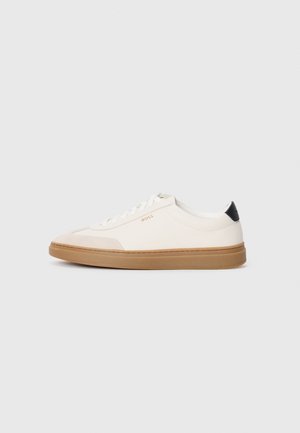 Des baskets blanches avec des accents beiges, un dessus en cuir lisse, un bout arrondi et une semelle en caoutchouc beige, avec une languette de talon noire et un branding subtil.