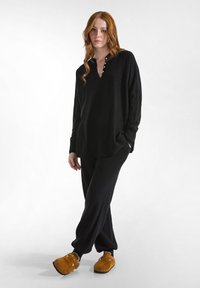 Zwarte gebreide langesleeve shirt met een knoopsluiting, gecombineerd met bijpassende zwarte losse broek en bruine instapklompen.
