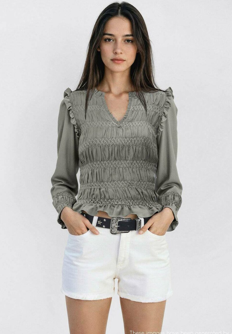 Siva bluzica s nabrusima na rukavima, V-izrezom, u kombinaciji s bijelim šortsevima. Bluzica ima teksturiranu površinu i pripijeni struk.