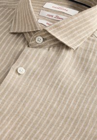 Camicia di lino con base beige chiaro e sottili righe bianche, con collo appuntito e bottoni bianchi. Etichette: "100% Lino" e "Reg".