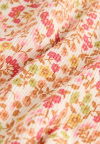 Mäkká rebrovaná látka s opakujúcim sa kvetinovým vzorom obsahujúcim ružové, žlté, zelené a hnedé kvety na smotanovom pozadí.