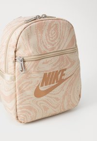 Rucsacul mini Nike din țesătură bej, cu un model texturat în spirală coraliu. Dispune de un compartiment principal cu închidere cu fermoar și un accent cu logo.