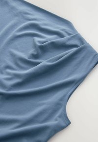 T-shirt bleu vu de dessus, mettant en avant un tissu doux avec une texture lisse, des plis drapés et une encolure ronde.