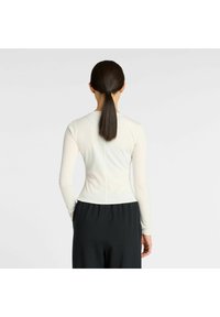 Lange mouwen top in crème, aansluitend ontwerp, met een gladde textuur en een ronde hem. Draag met zwarte high-waisted onderkleding, die een naadloze achterkant toont.