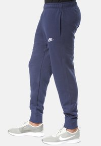 Marinblåa sweatpants med elastisk midjeband, sidofickor och vit Nike-logotyp. Bomullsblandat tyg med slät textur. Figursydda ankelfållar.