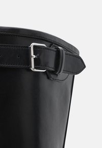 Borsa a secchiello in pelle nera con una texture liscia. Presenta una chiusura in metallo argentato e dettagli cuciti lungo il bordo superiore e la tracolla.