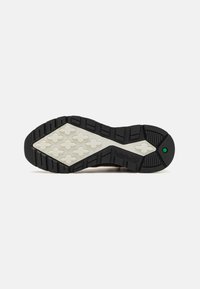 Gummisohle des Sneakers mit einem robusten, strukturierten schwarzen Design. Verfügt über eine kontrastierende weiße Zwischensohle mit geometrischen Mustern und einem grünen Akzent.