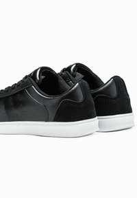 Sneaker nere con upper in pelle liscia e camoscio, suola in gomma bianca, punta arrotondata e minimo dettaglio di perforazione sui lati.