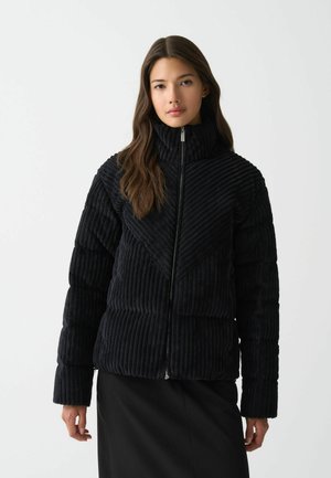 Zwarte corduroy jas met verticale ribbeltextuur, hoge kraag, ritssluiting en een geometrisch ontwerp aan de voorkant. Lange mouwen.