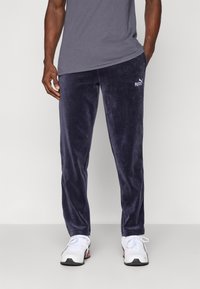 Ναυτικό βελούδινα joggers με ελαστική μέση. Περιλαμβάνει το λογότυπο της Puma στο δεξί μηρό. Συνδυάζεται με άσπρα αθλητικά παπούτσια.