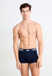 Tamsiai mėlynos vyriškos boxer tipo trumpikės, pritaikytos, pagamintos iš tamprus audinio, su balta prekinio ženklo elastinga juosta.