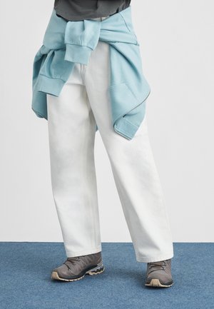 Biele široké nohavice, sivé športové topánky s textúrovaným zvrškom a svetlomodrá mikina zviazaná okolo pása. Jednoduchý dizajn, bez vzorov.