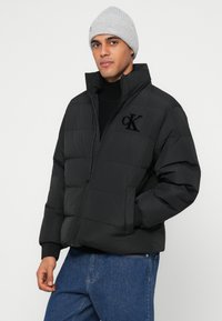 Fekete steppelt dzseki cipzárral az elején, magas gallérral és hímzett "cK" logóval. Vastag, steppelt kialakítás bordázott mandzsettával.