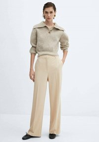 Beige wijde broek in combinatie met een licht taupe gebreide trui met kraag en knoop. De textuur lijkt zacht en gezellig.