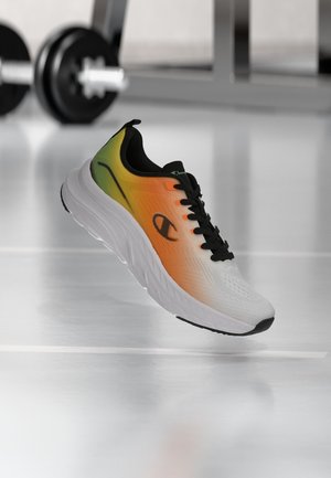 Laufschuh mit weißer Sohle und Farbverlauf im Obermaterial in Gelb, Orange und Grün, schwarzen Schnürsenkeln und einem schwarzen Logo an der Seite, vor einem Hintergrund mit Fitnessgeräten.