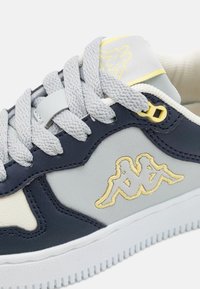Marineblauwe en lichtgrijze sneaker van gestructureerd leer, met witte zool, grijze veters en gele geborduurde logo-accenten. Laag model.