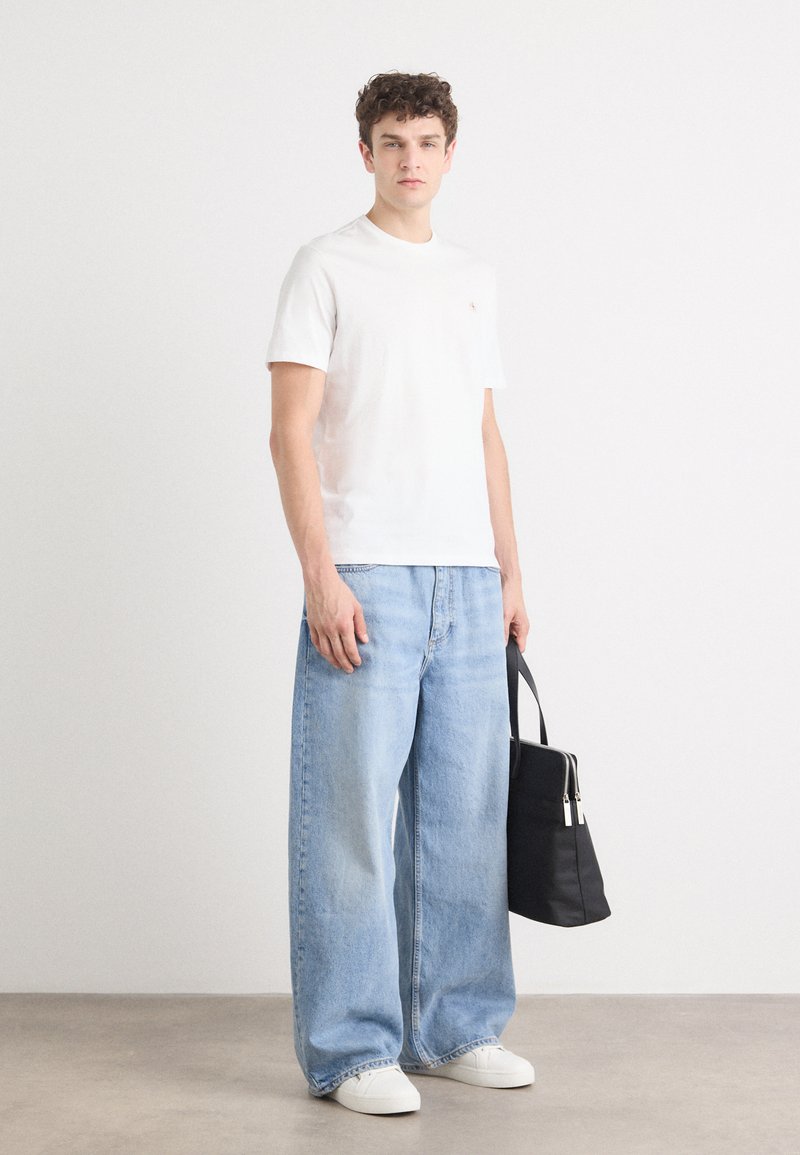 Camiseta blanca de manga corta, jeans de pierna ancha azul claro y zapatillas blancas. Sosteniendo un bolso negro con detalles plateados. Texturas de tela suaves.