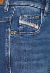 Denim jeans back pocket with Diesel Industry label and brass rivet detailing on blue faded denim fabric.