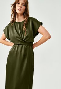 Olivnozeleni satenski obleka s kratkimi rokavi, s preševnim dizajnom na pasu in ravno silhueto. Gladka tekstura z rahlim sijajem.