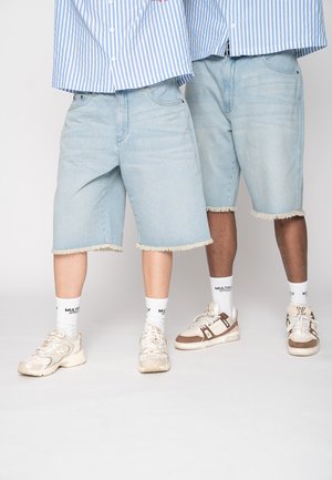 Zwei Personen tragen hellblaue Jeansshorts mit ausgefransten Säumen, weiße Socken, Turnschuhe und blau gestreifte Hemden.