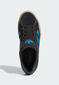 Čierna semišová teniska s tromi modrými pruhmi, čiernymi šnúrkami a svetlohnedou gumovou podrážkou. Navrhnutá na bežné nosenie s zaoblenou špičkou.