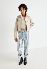 Beige kort jakke, tettsittende lys topp, glinsende sølv løse jeans, rullet mansjetter og svarte ankelstøvler. Teksturerte materialer vises.