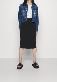 Jeansjacka, åtsittande vit t-shirt, svart blyertskjol och svarta platta slidesandaler. Jackan har knapplist och bröstfickor.