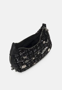 Sac en tweed noir et blanc avec des accents en cuir, doté d'un quincaillerie en métal argenté et d'ornements décoratifs. Fermeture éclair en haut.